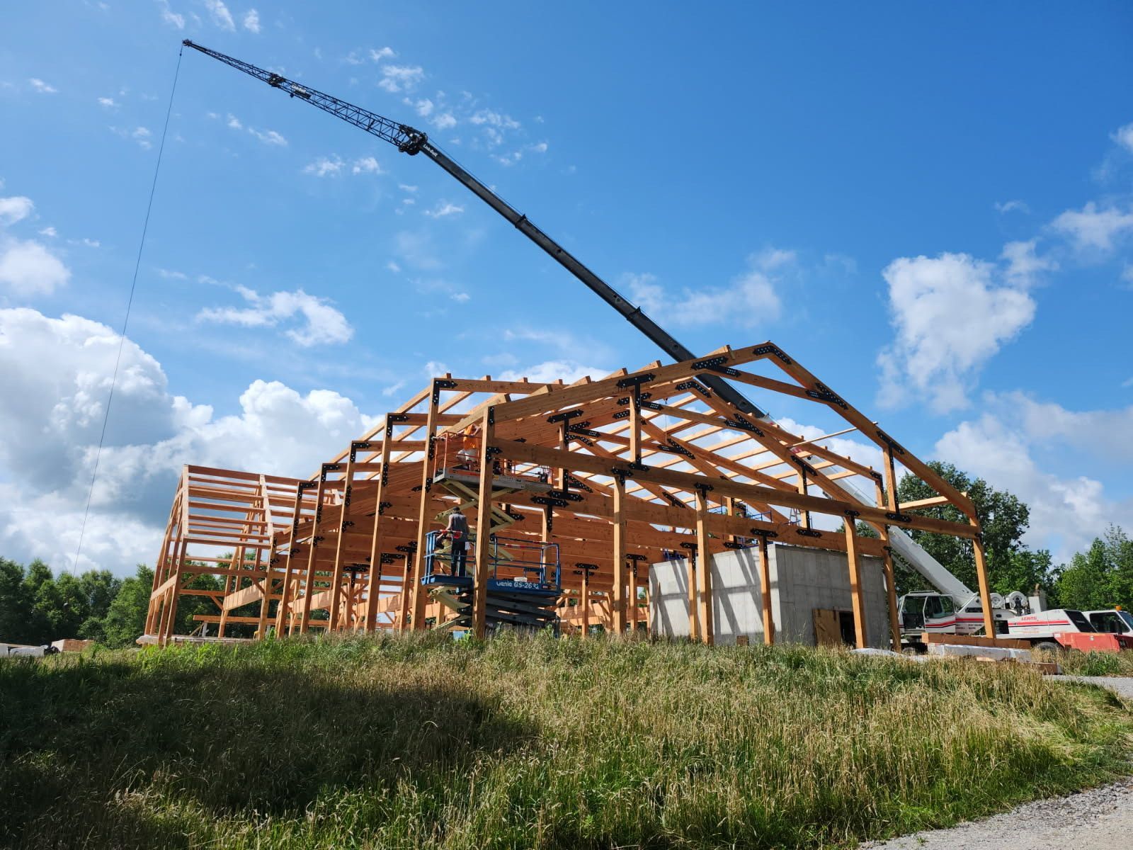 Construction site with large wooden frame being built; crane lifting; blue sky.
