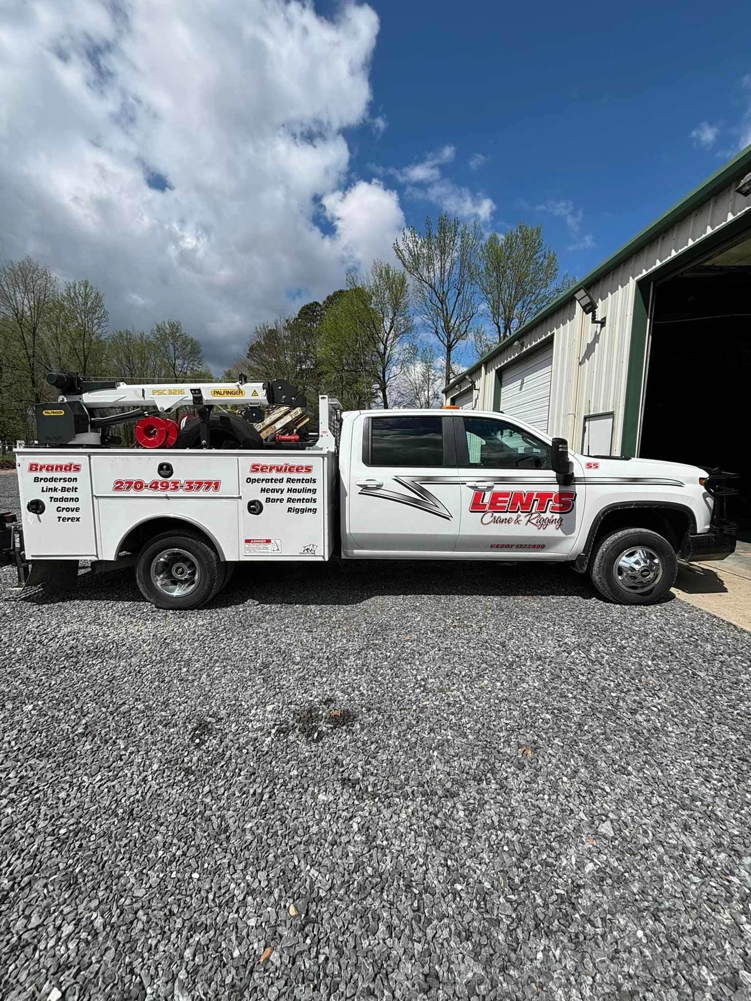 A white truck is parked in a gravel lot in front of a building.