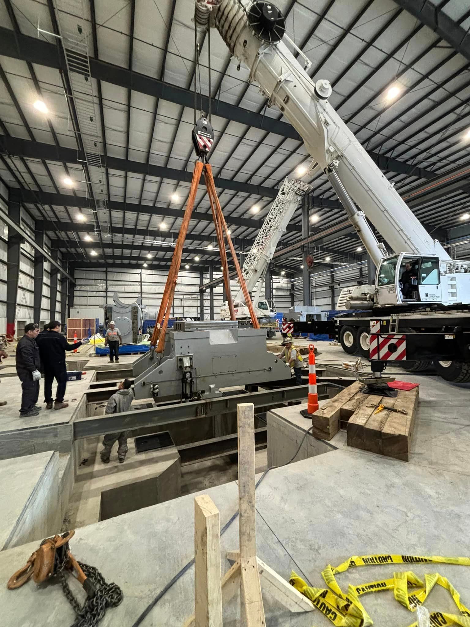 A large crane is lifting a piece of metal in a large building.