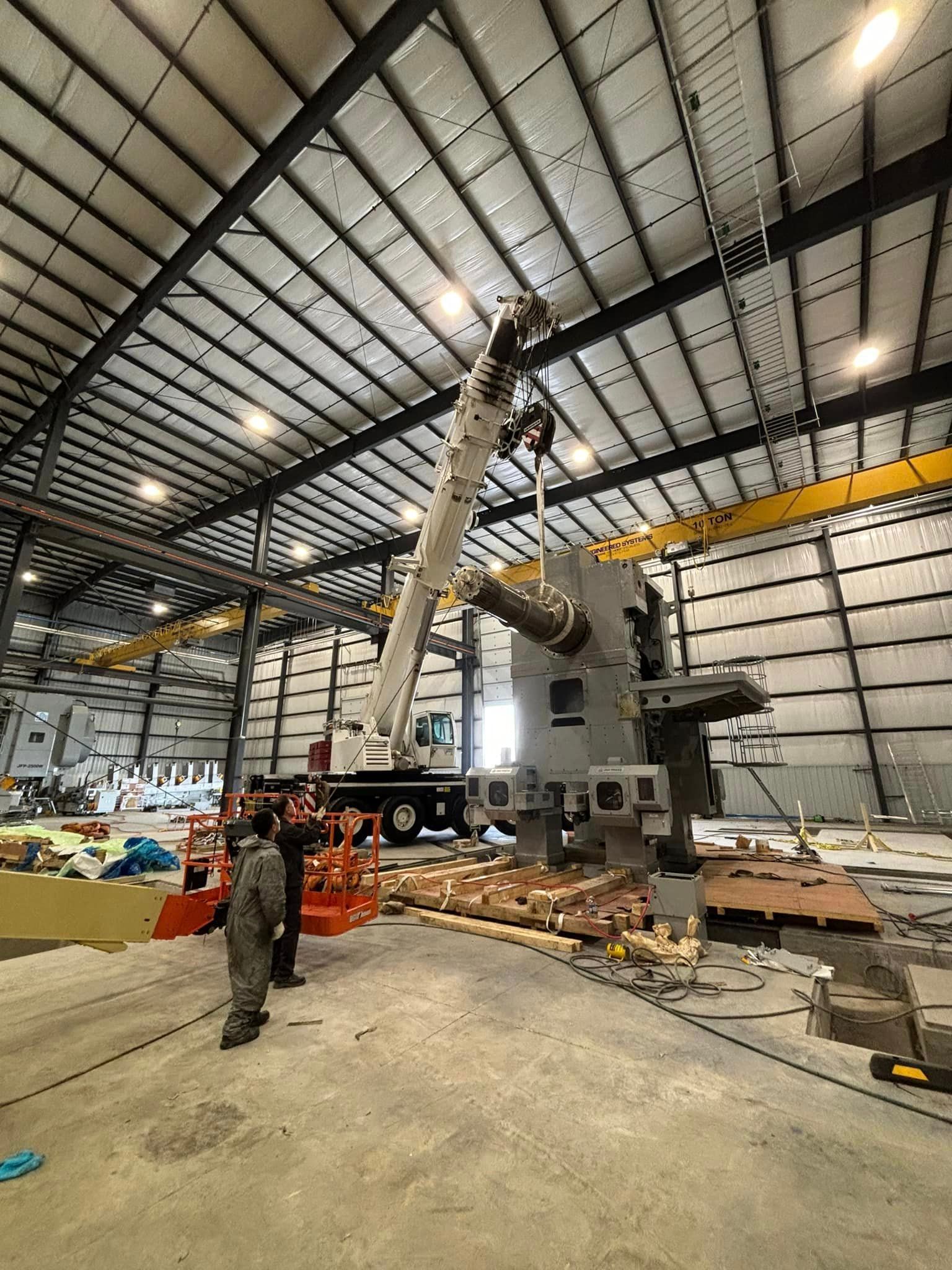 A large machine is being lifted by a crane in a large warehouse.