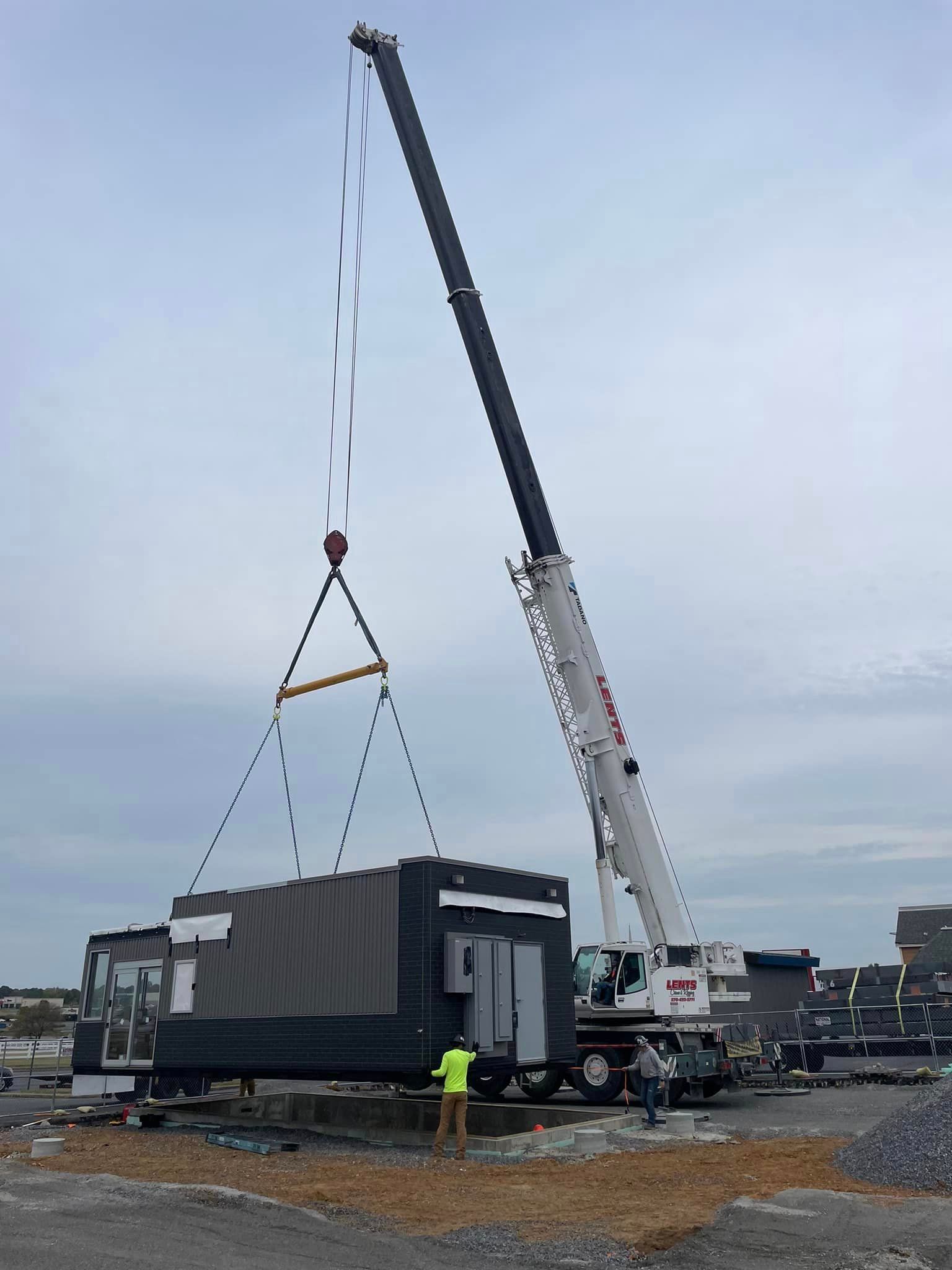 A large crane is lifting a container in a parking lot.