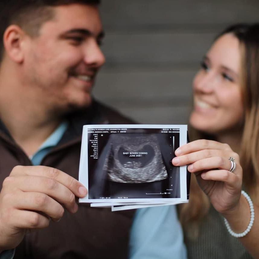 A man and a woman are holding a picture of a baby