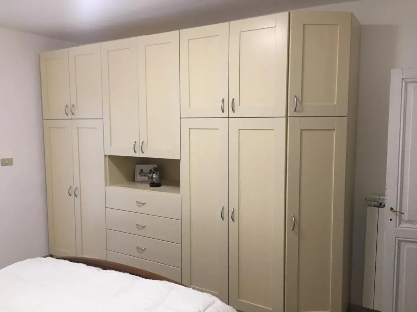 Armadio a muro color crema con più ante, cassetti e una piccola cassaforte, situato in una camera da letto.