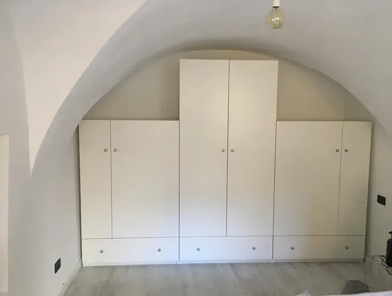 Armadio a muro bianco contro un soffitto a volta. L'armadio ha diverse ante e cassetti.