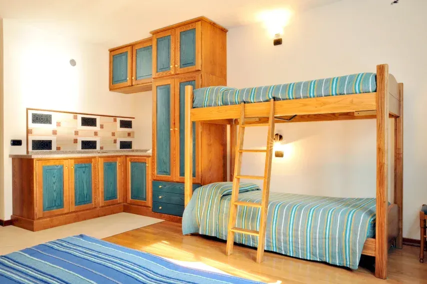 Letto a castello in una stanza con mobili in legno e dettagli blu. Include una scala, letti e un angolo cottura.