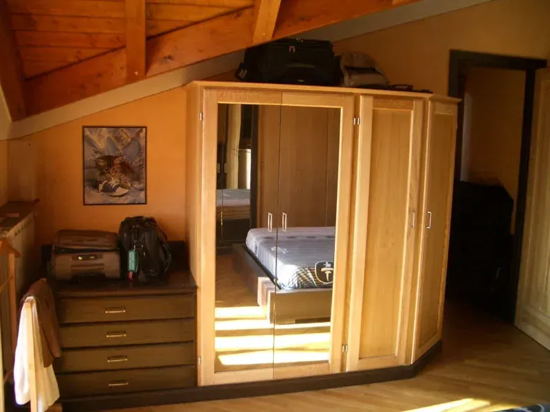 Camera da letto con armadio in legno chiaro con ante a specchio, cassettiera, opere d'arte e soffitto in legno a vista.