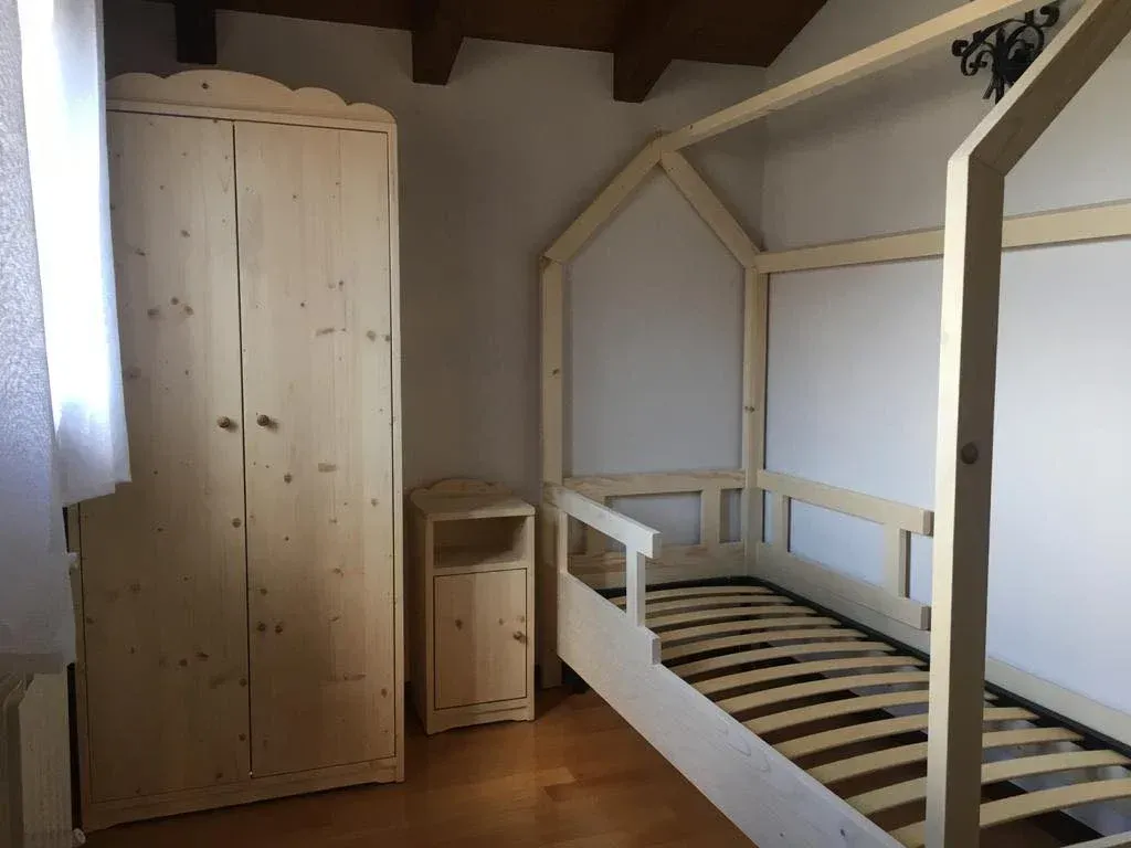 Mobili in legno chiaro in una camera da letto: un armadio, un comodino e un letto con struttura a doghe.