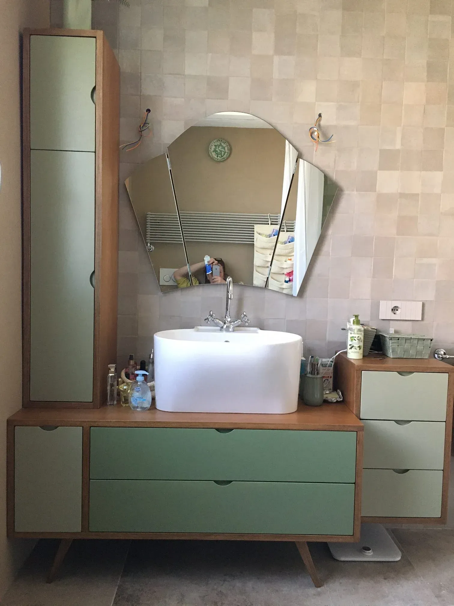 Bagno moderno con mobili verdi, lavandino bianco e specchio geometrico.