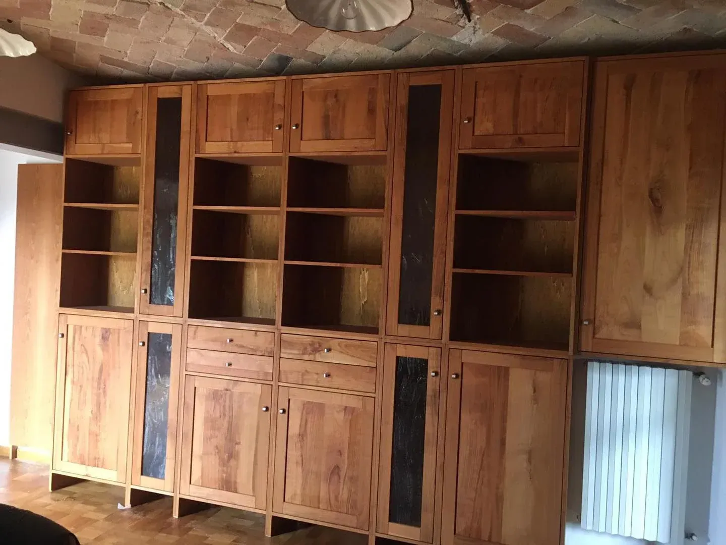 Armadi in legno a muro con ripiani aperti e ante chiuse; soffitto in mattoni; interno della stanza.