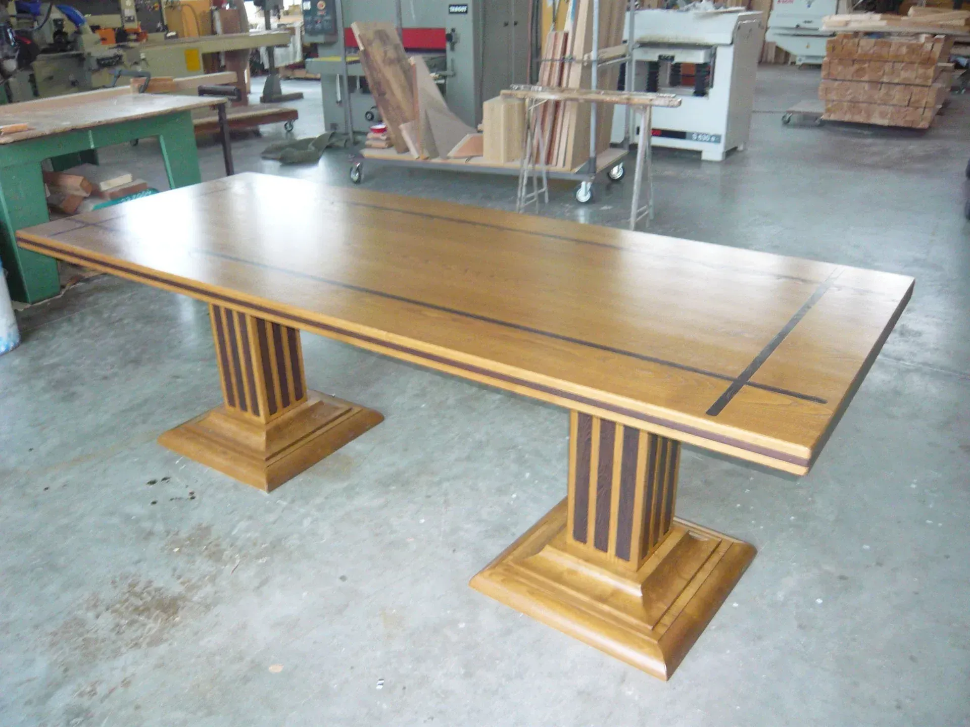 Tavolo da pranzo in legno con piano rettangolare e due basi a piedistallo in un laboratorio.