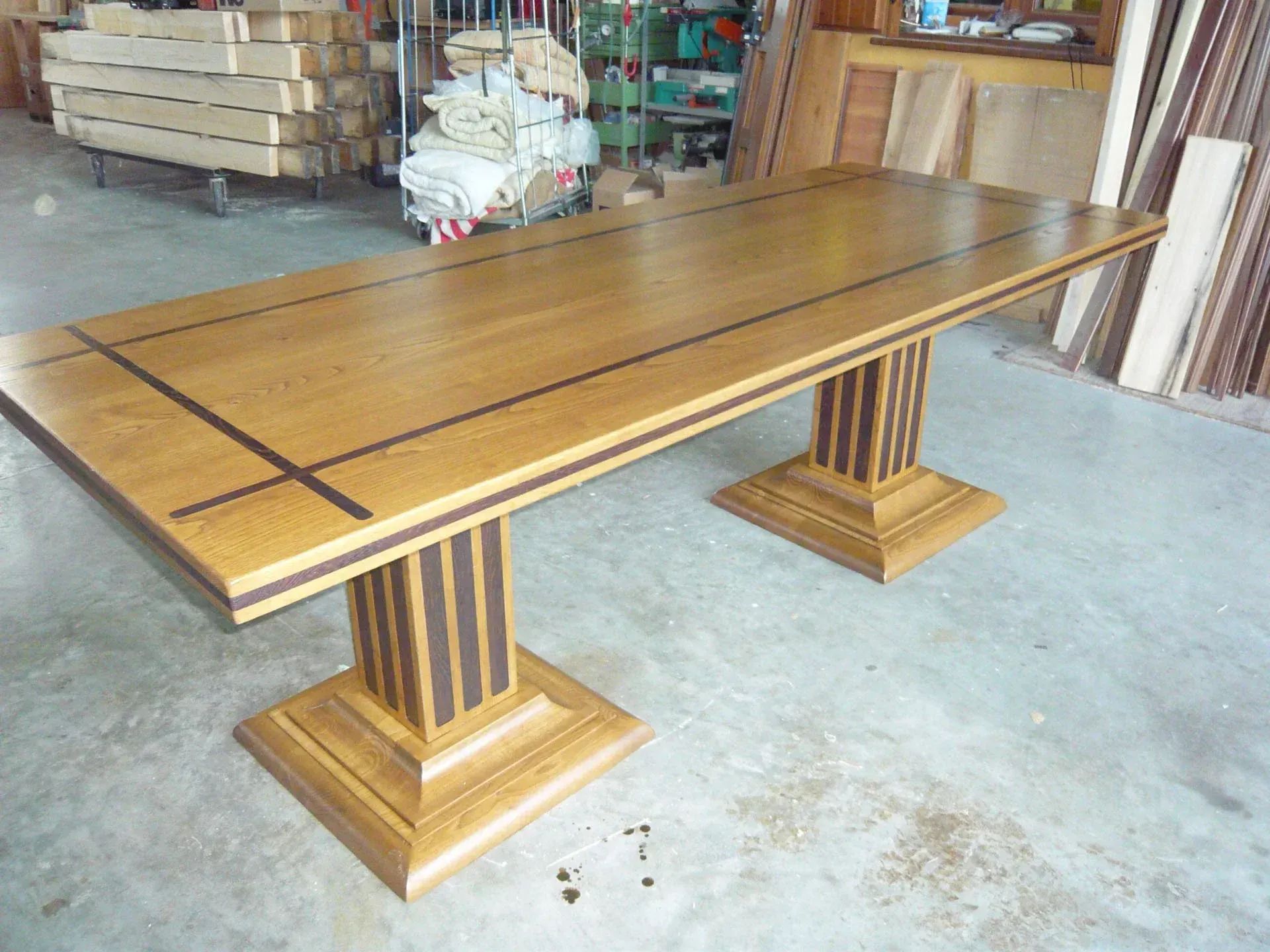 Tavolo da pranzo rettangolare in legno con due basi a piedistallo, marrone e legno chiaro, in un ambiente da laboratorio.