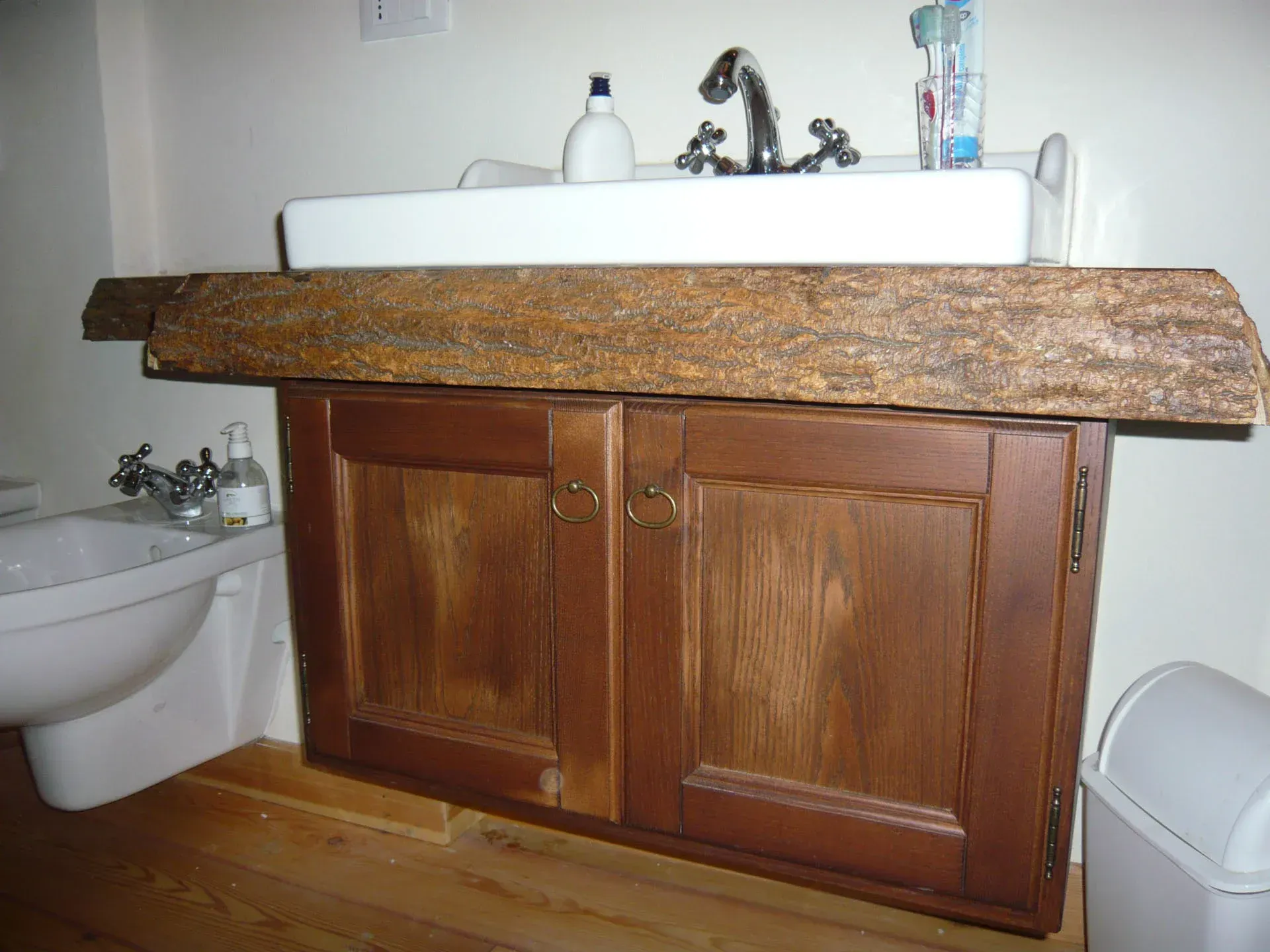 Mobiletto del bagno con mobili in legno scuro e una trave spessa e ruvida che sostiene un lavandino bianco.