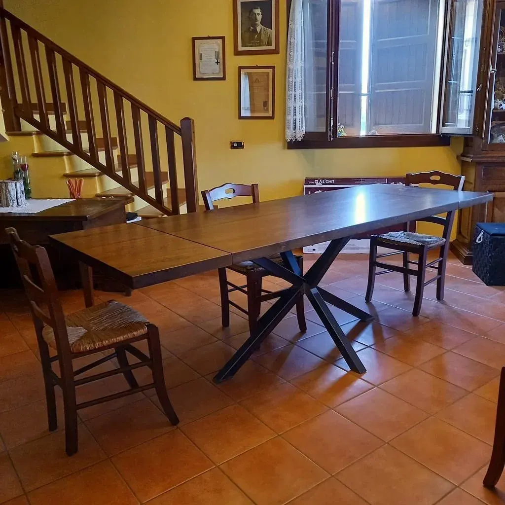 Sala da pranzo con un lungo tavolo in legno, sedie, scala e finestra.