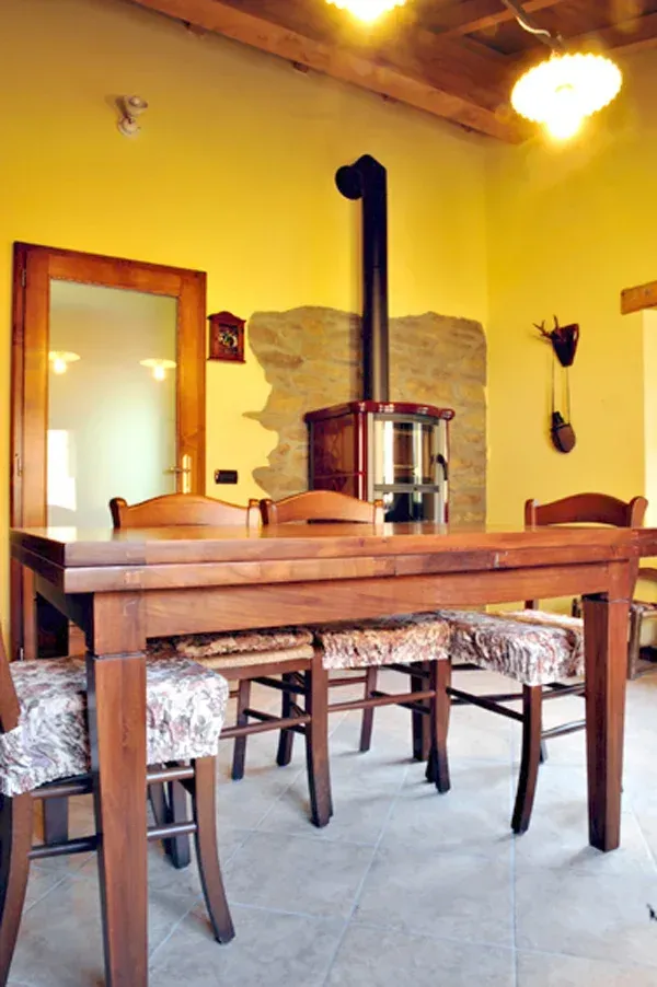 Tavolo da pranzo in legno e sedie di fronte a un muro in pietra con una stufa a legna e uno specchio.