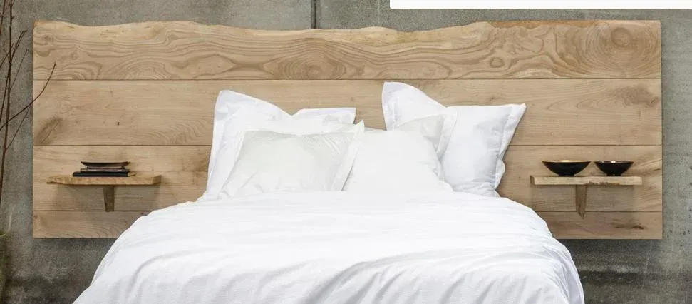 Camera da letto con testiera in legno, biancheria da letto bianca e piccole mensole con ciotole decorative.
