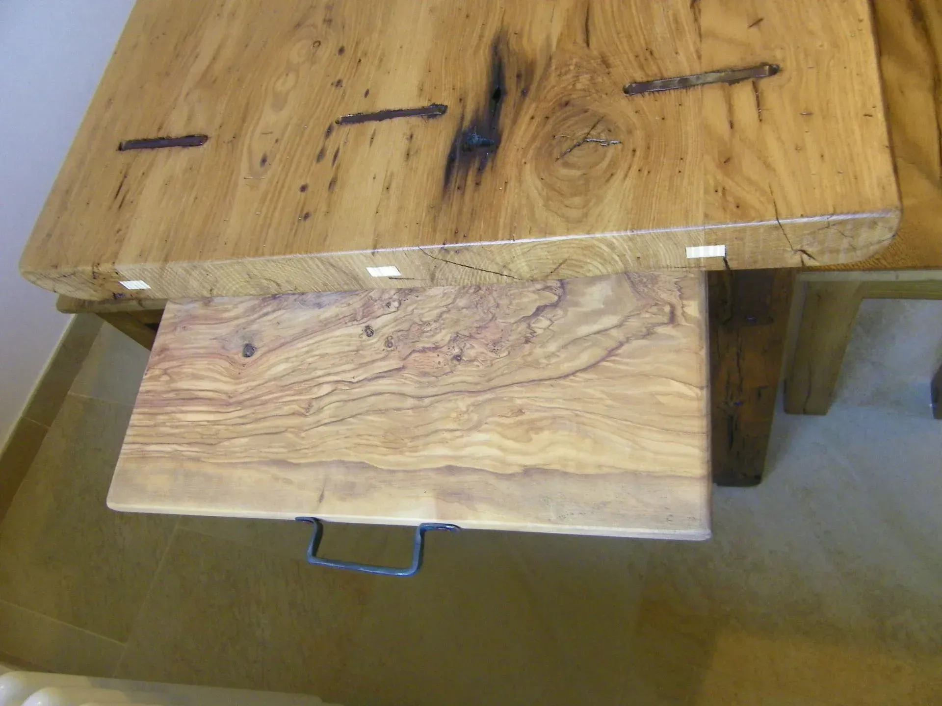 Tavolo in legno con cassetto estraibile, venature del legno e ferramenta in metallo.