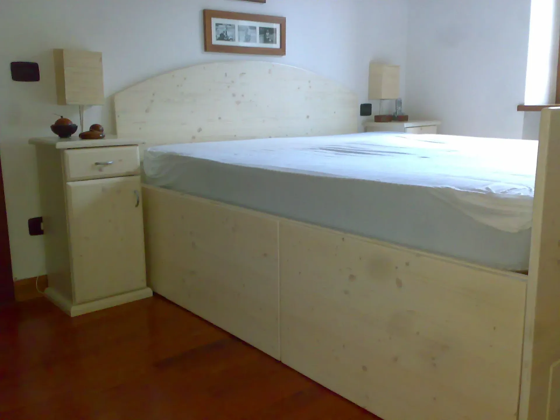 Camera da letto bianca con letto, comodini e testiera contro una parete bianca.