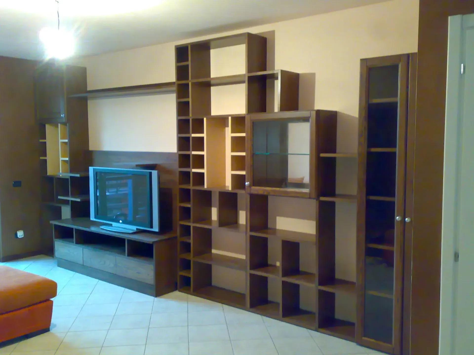 Soggiorno con scaffalature in legno scuro, TV e divano arancione.