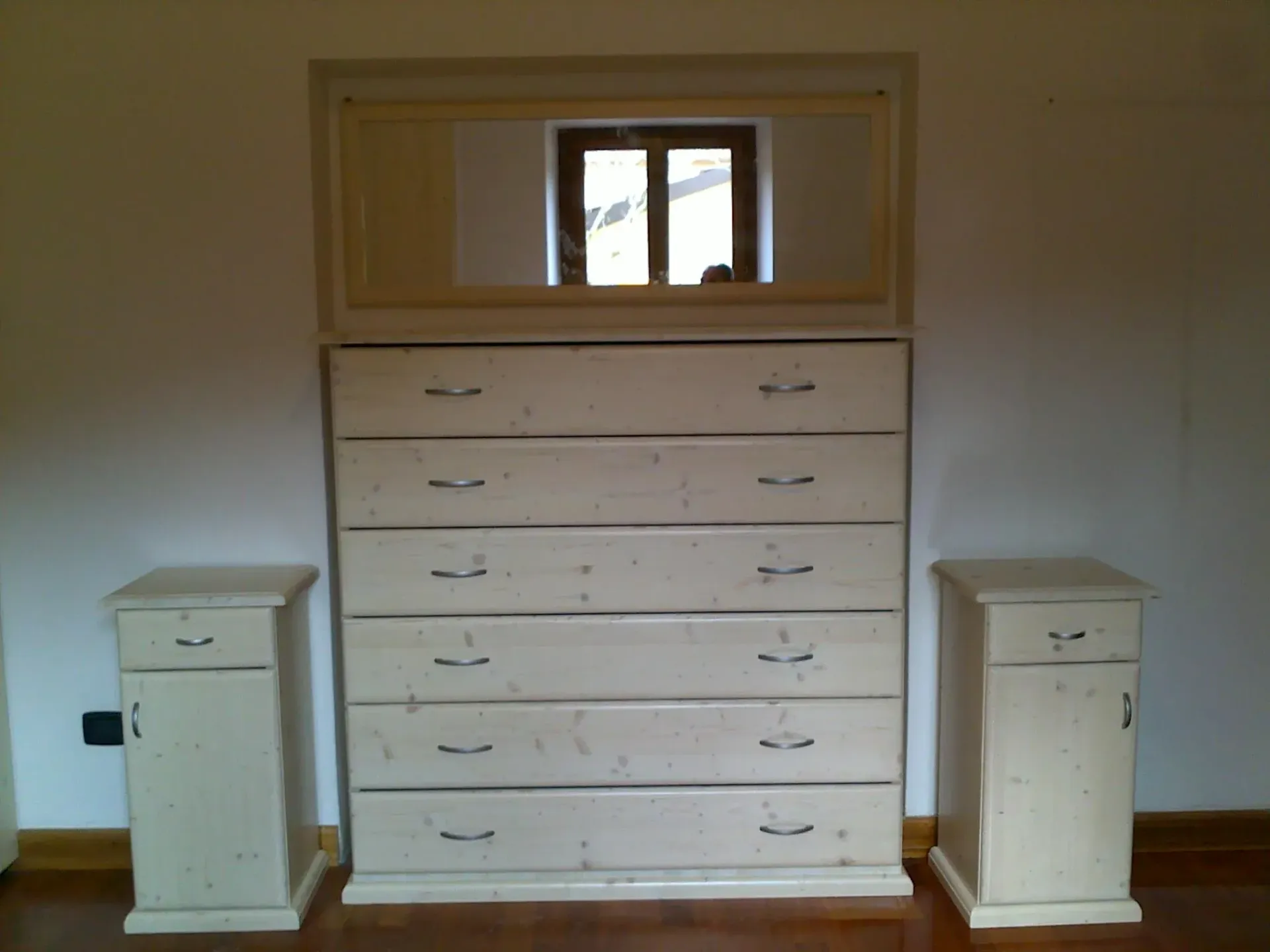 Un'alta cassettiera bianca con uno specchio sopra, affiancata da due comodini coordinati, il tutto in una stanza.