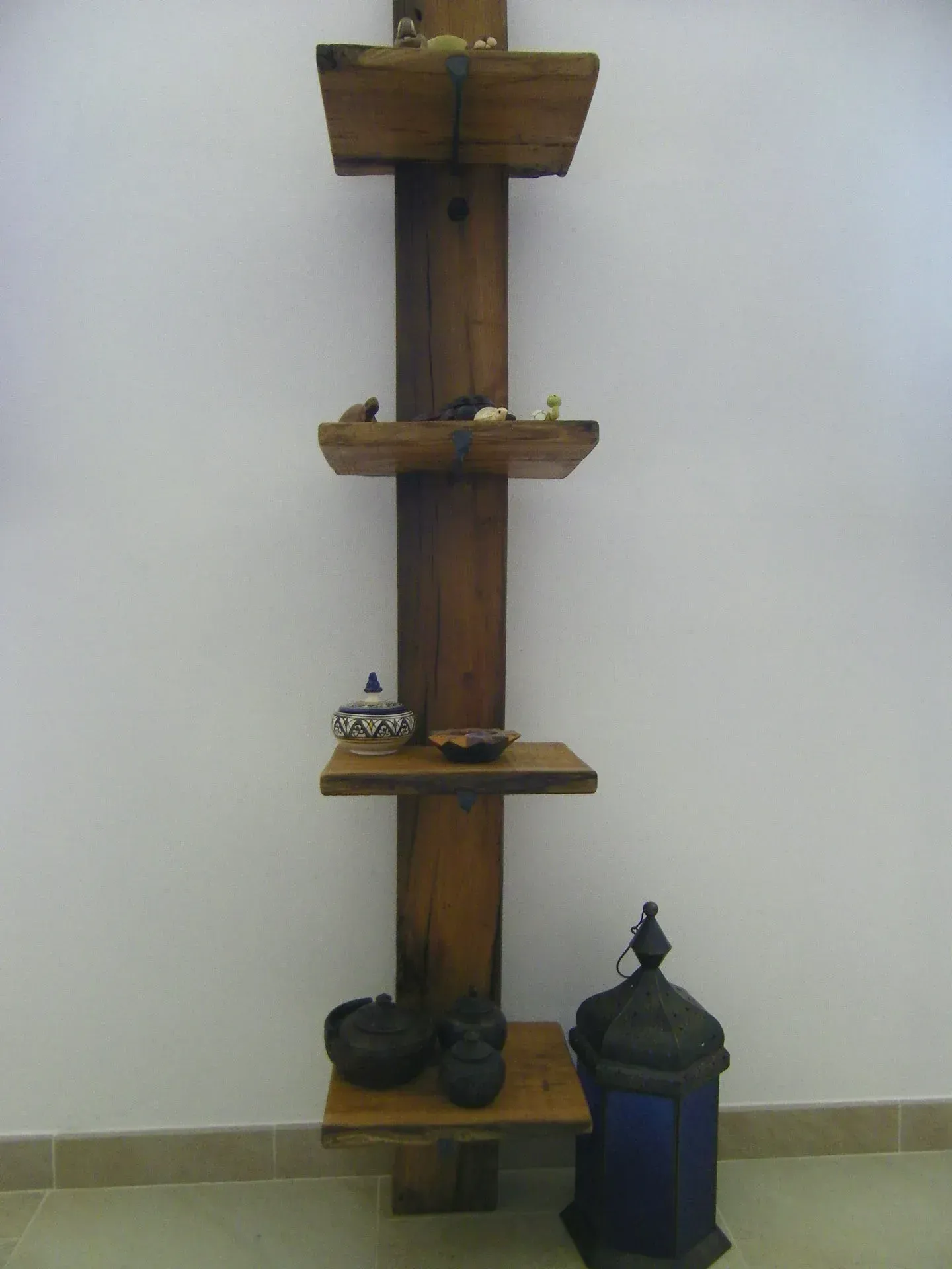 Scaffale in legno contro una parete bianca; contiene vari piccoli oggetti e una lanterna.