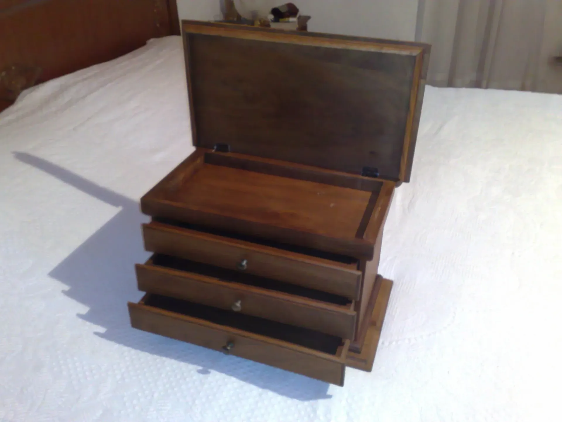 Cassettiera in legno con tre cassetti e coperchio incernierato, aperta su una superficie bianca.