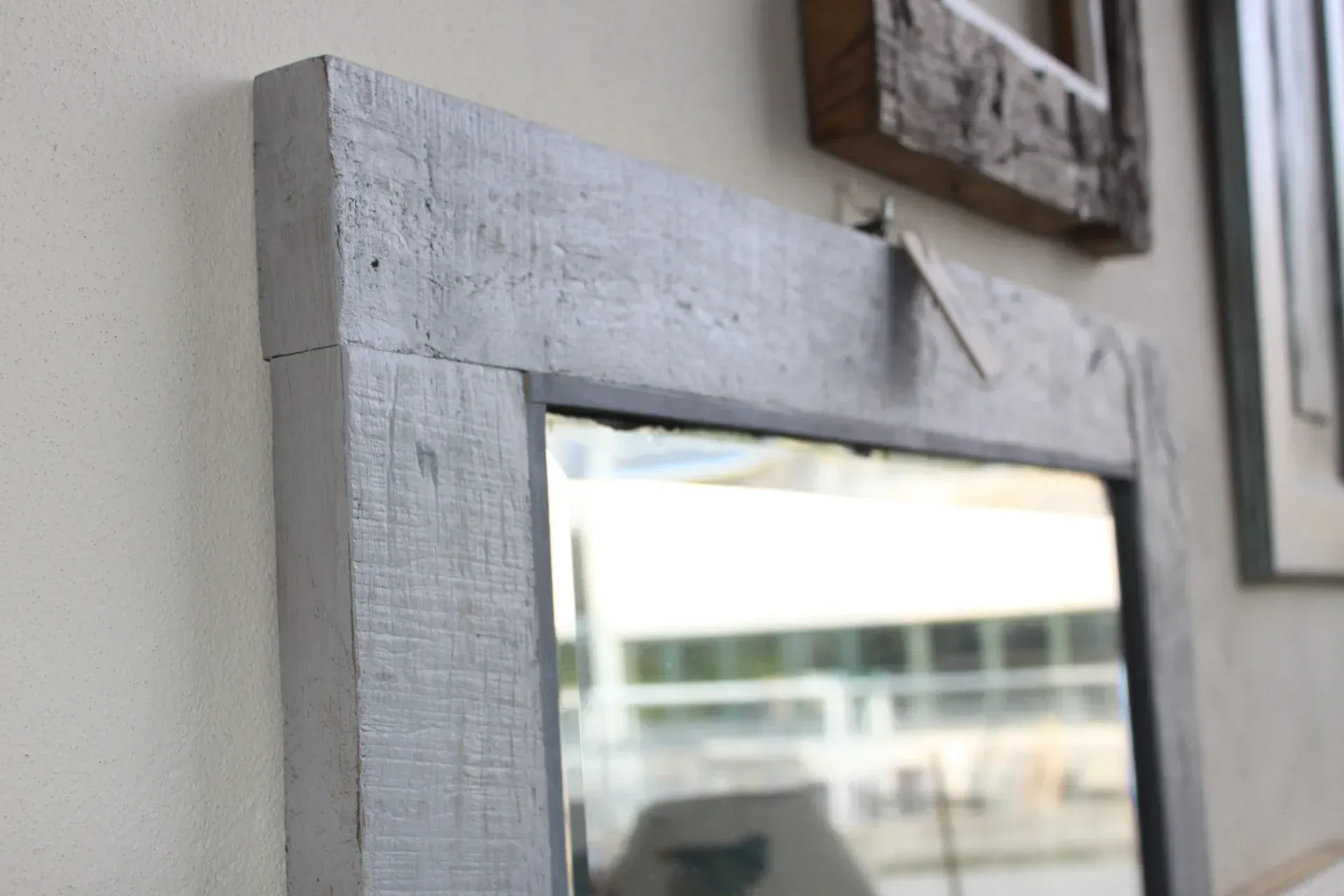 Specchio con cornice grigia appeso a una parete bianca, altre cornici sullo sfondo.