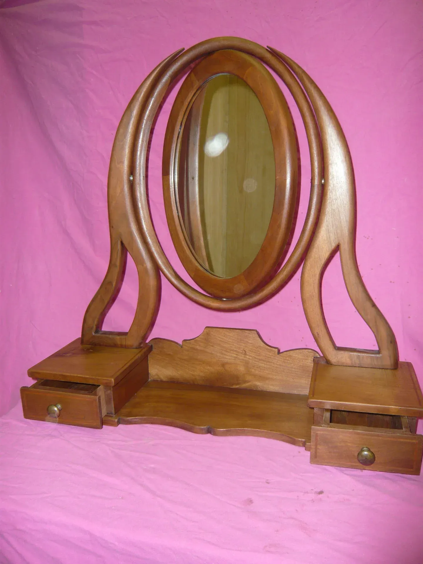 Specchio ovale in legno con cassetti, su sfondo in tessuto rosa.