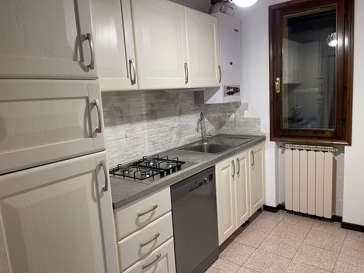 Cucina con mobili, isola ed elettrodomestici color verde menta e grigio; pareti bianche e una finestra.