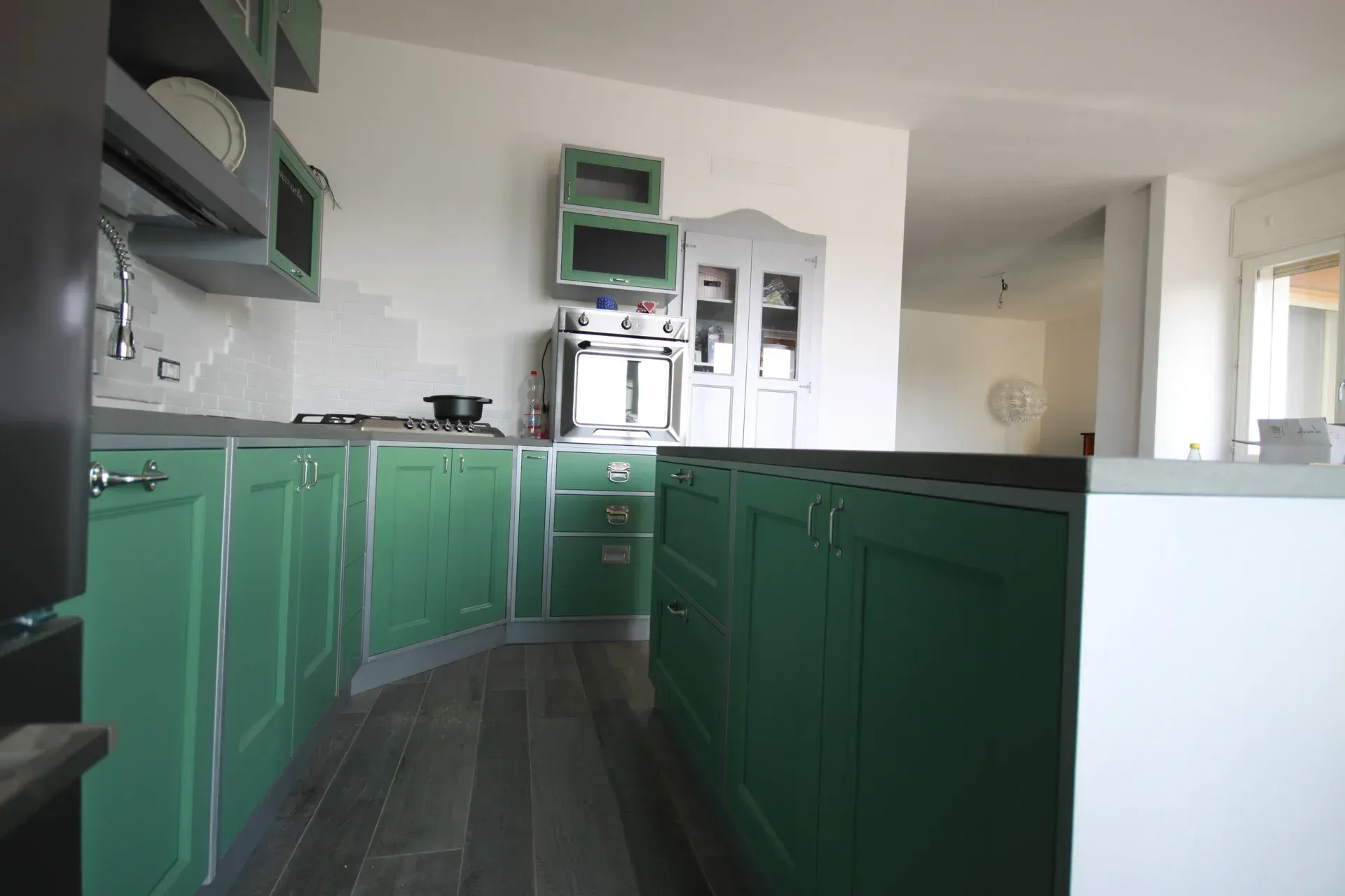 Cucina verde con mobili, fornelli e isola. Pavimento grigio, pareti bianche.