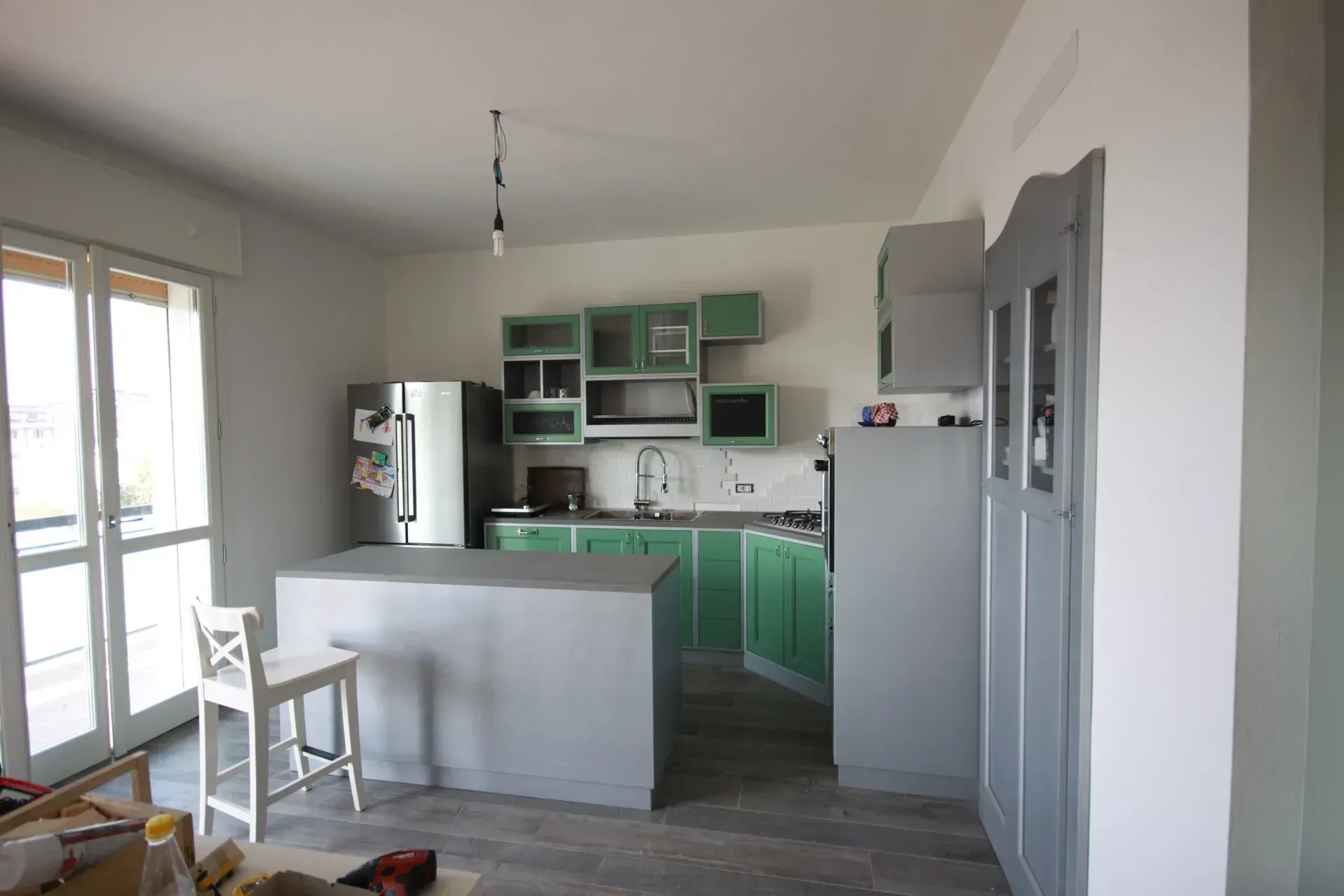 Cucina con mobili, isola ed elettrodomestici color verde menta e grigio; pareti bianche e una finestra.