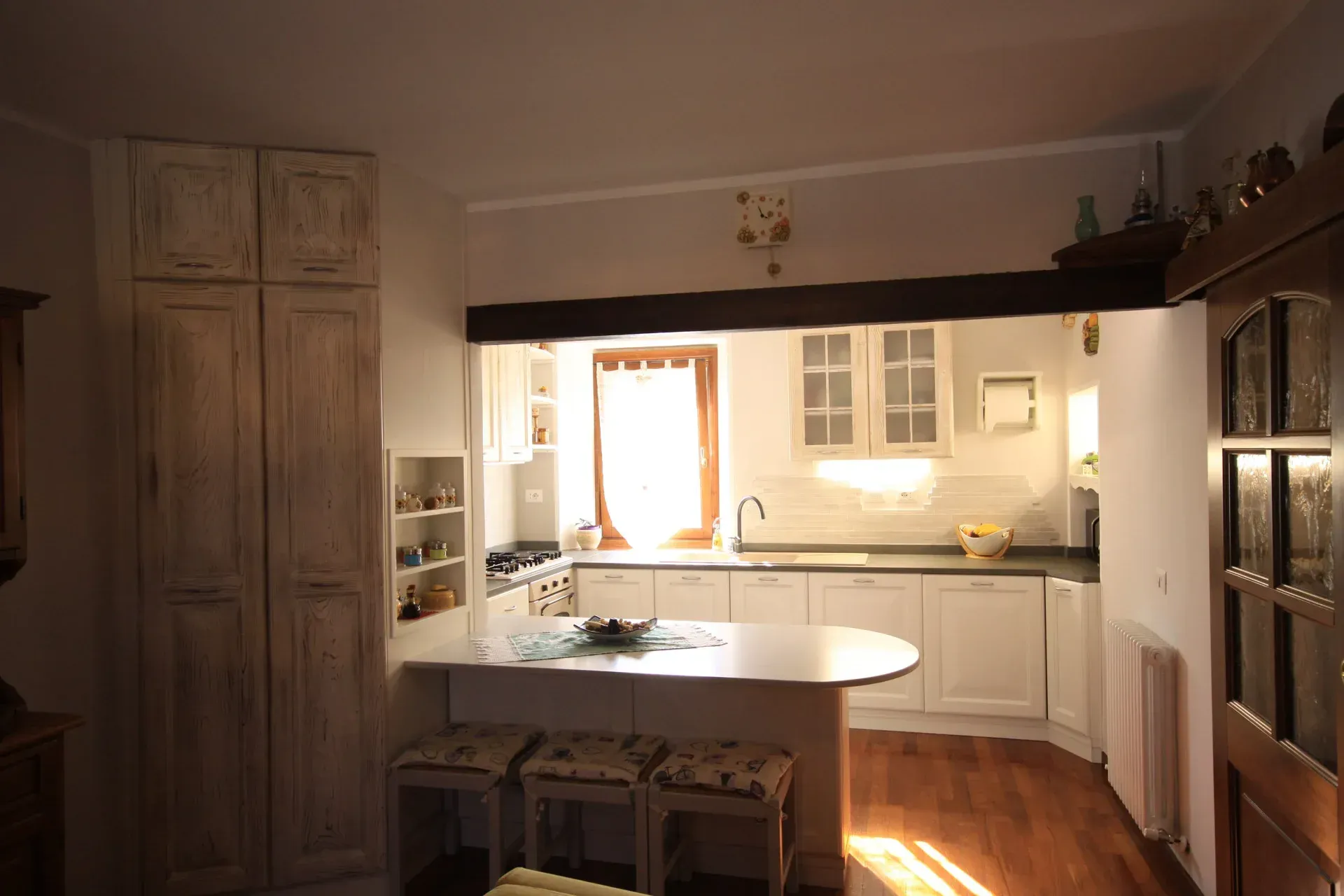Cucina bianca con bancone per la colazione, mobili in legno e una finestra con luce naturale.
