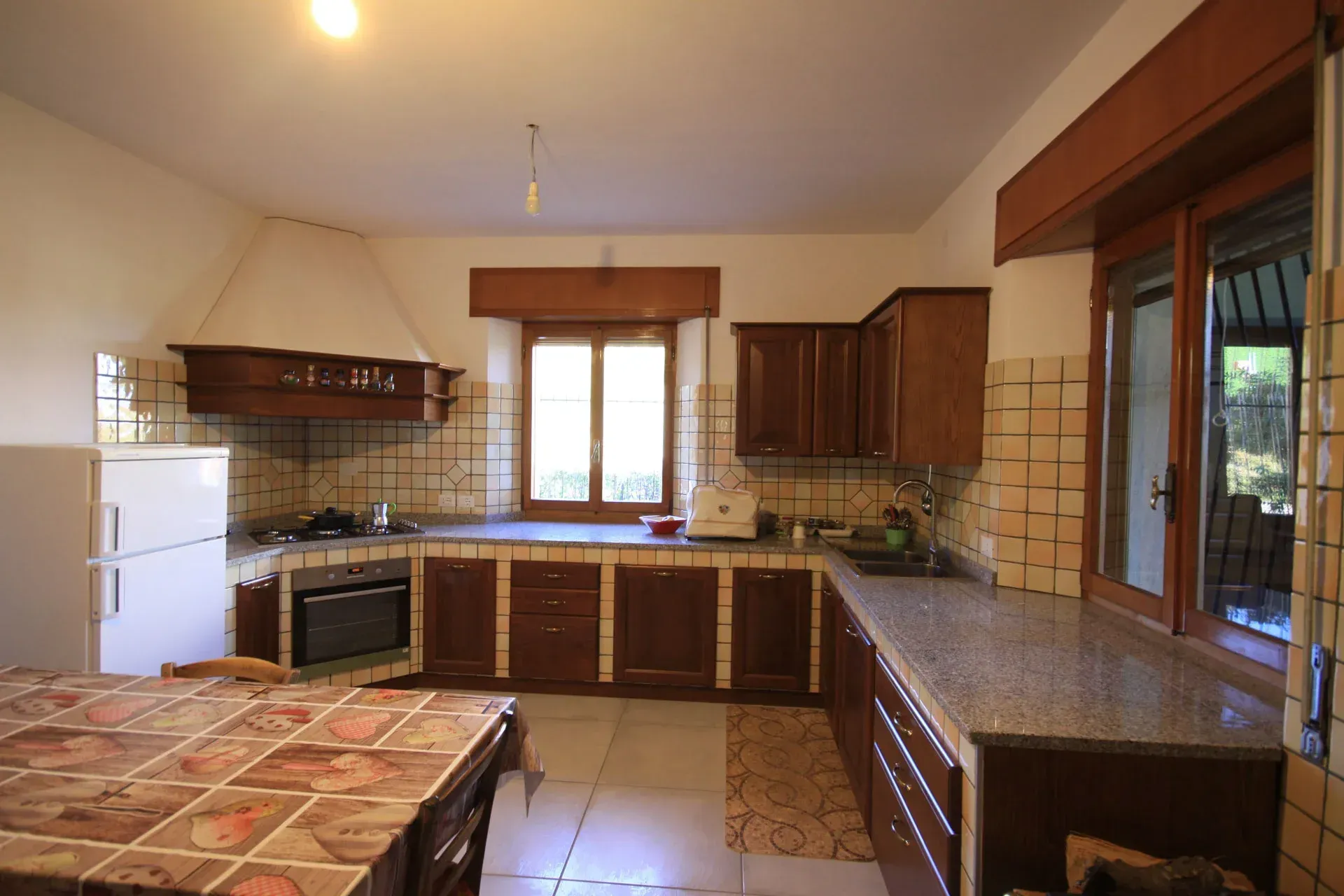 Cucina con mobili in legno scuro, ripiani in granito, paraschizzi e pavimento piastrellati.