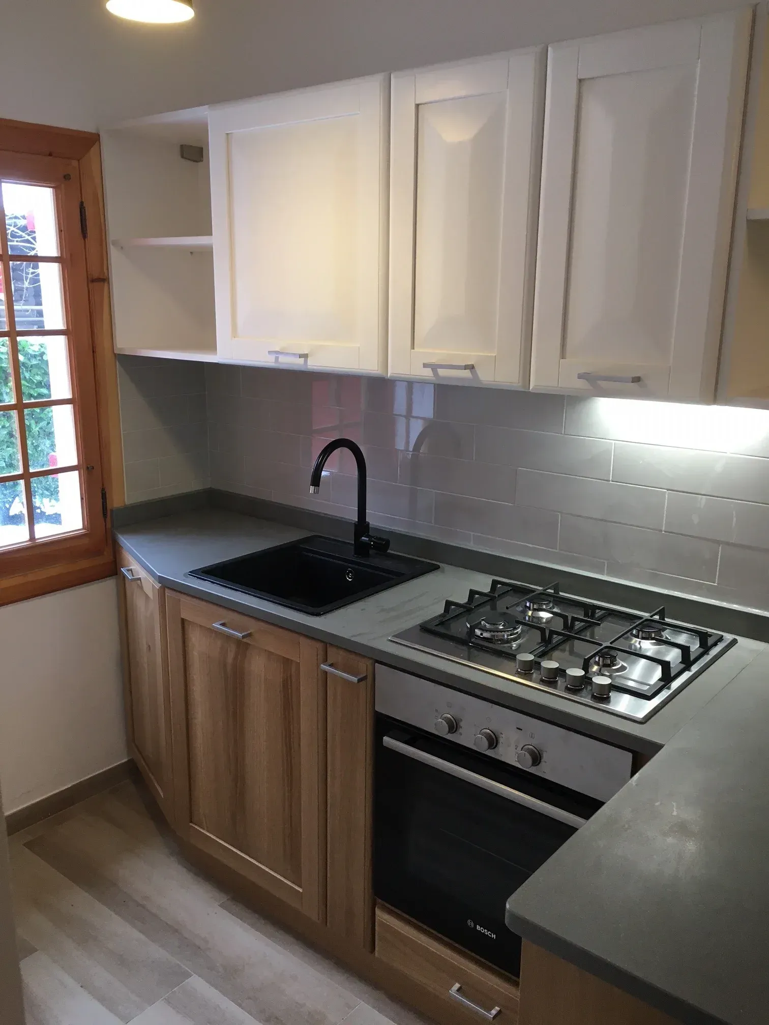 Cucina con pensili bianchi, pensili in legno, lavello ed elettrodomestici neri.