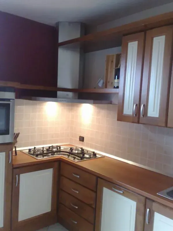 Cucina con mobili in legno, fornello a gas e cappa in acciaio inox, dotata di illuminazione calda.