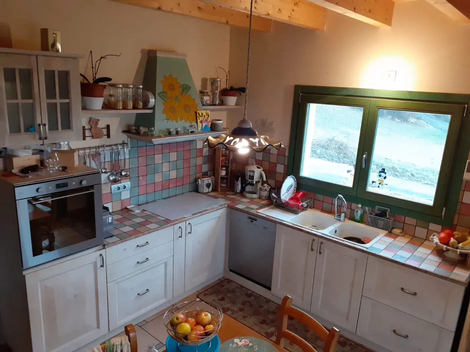 Cucina con mobili bianchi, paraschizzi piastrellato, grande finestra con finiture verdi e forno.