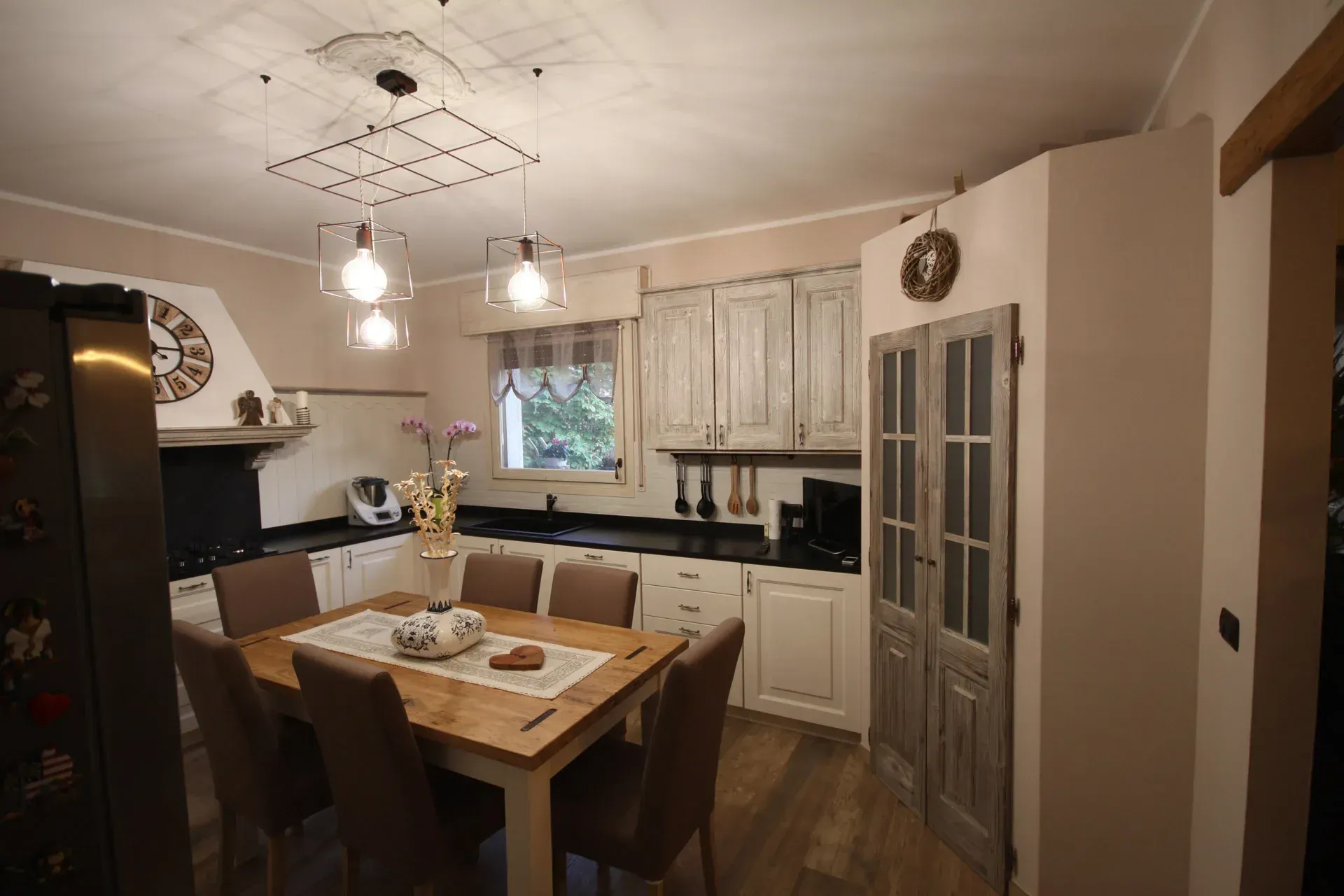 Cucina con tavolo in legno, mobili bianchi e lampade in stile vintage.