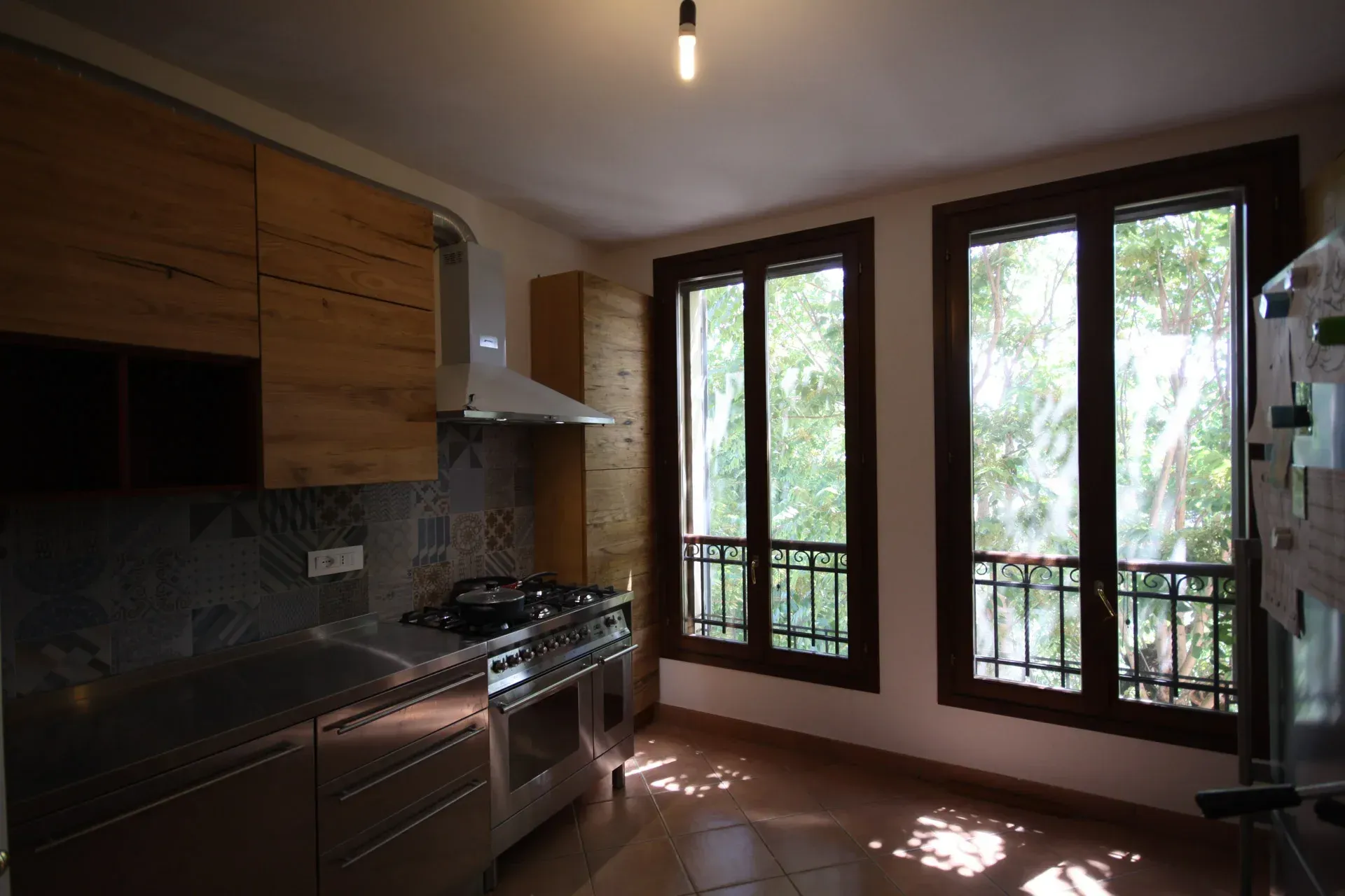 Cucina con mobili in legno, elettrodomestici in acciaio inossidabile e finestre con vista sul verde.