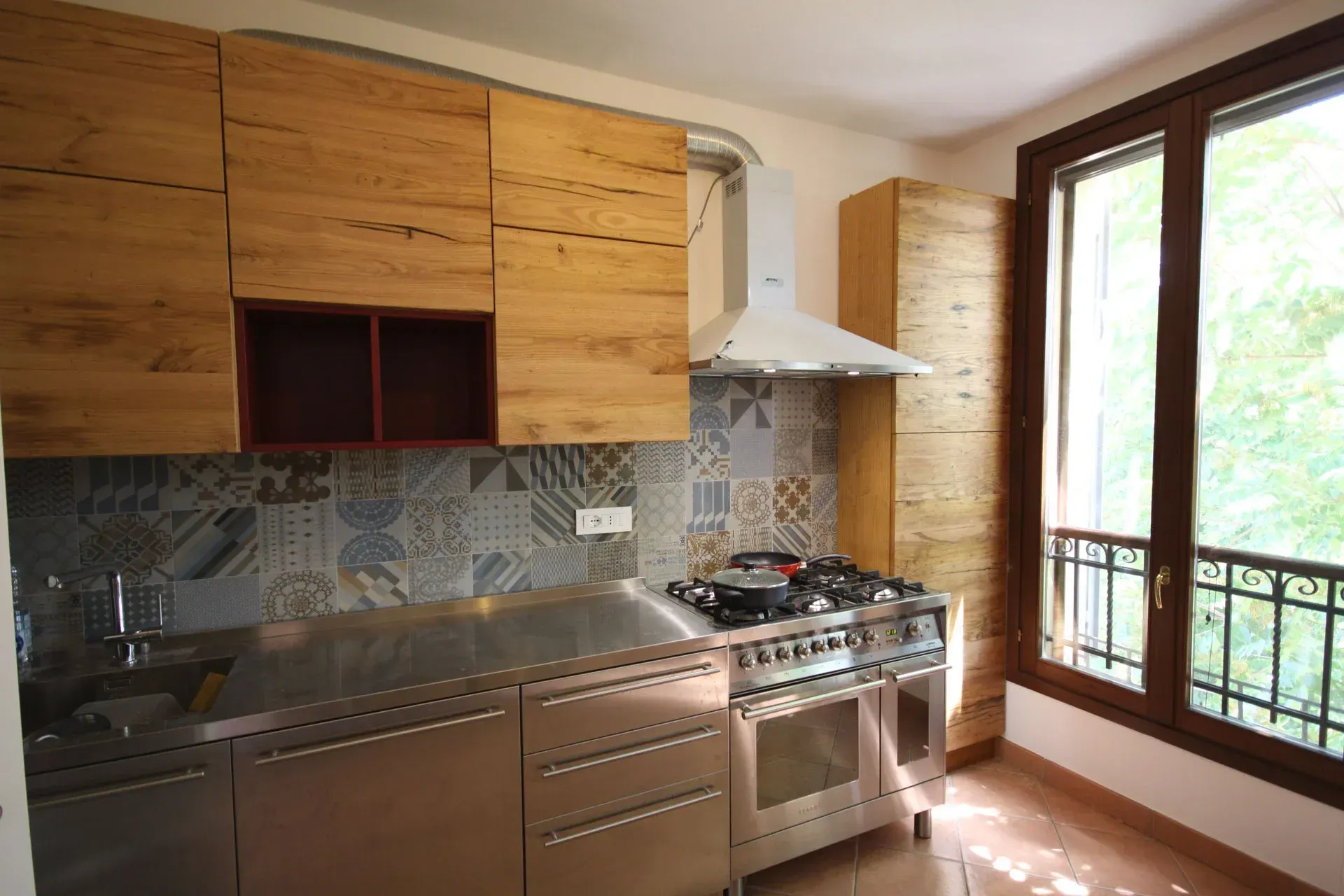 Cucina con mobili in legno, elettrodomestici in acciaio inossidabile e paraschizzi in piastrelle decorate.