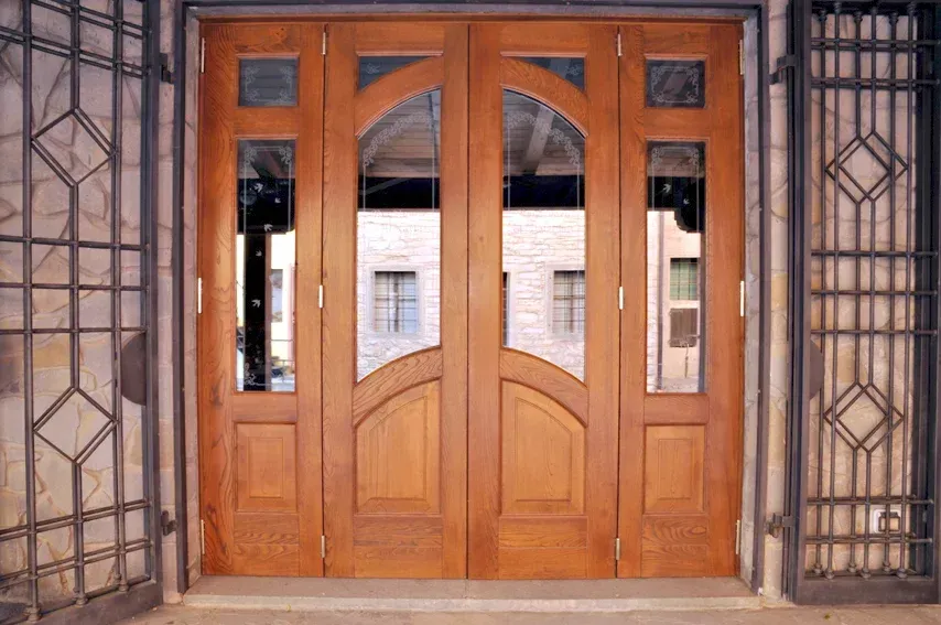 Doppie porte in legno con pannelli in vetro ad arco, inserite in una facciata in pietra.