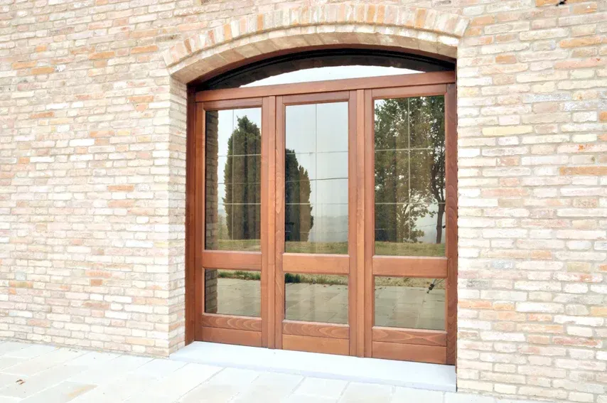 Porte in legno con pannelli in vetro inseriti in un arco in mattoni.