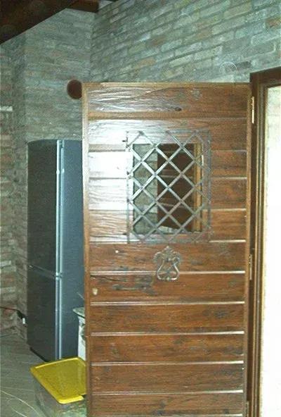 Porta in legno con finestra e maniglia in ferro battuto, inserita in una stanza in mattoni e pietra accanto a un frigorifero.