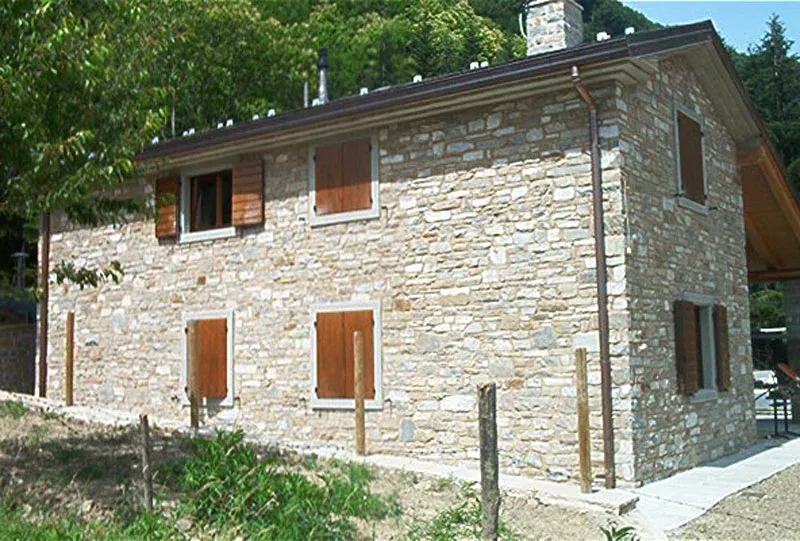 Casa in pietra con persiane e tetto marroni, immersa in un ambiente verde e naturale.