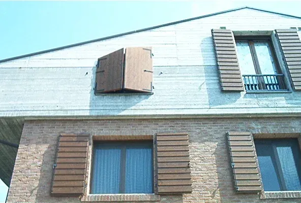 Persiane in legno marrone su un edificio in mattoni, con una persiana parzialmente aperta.