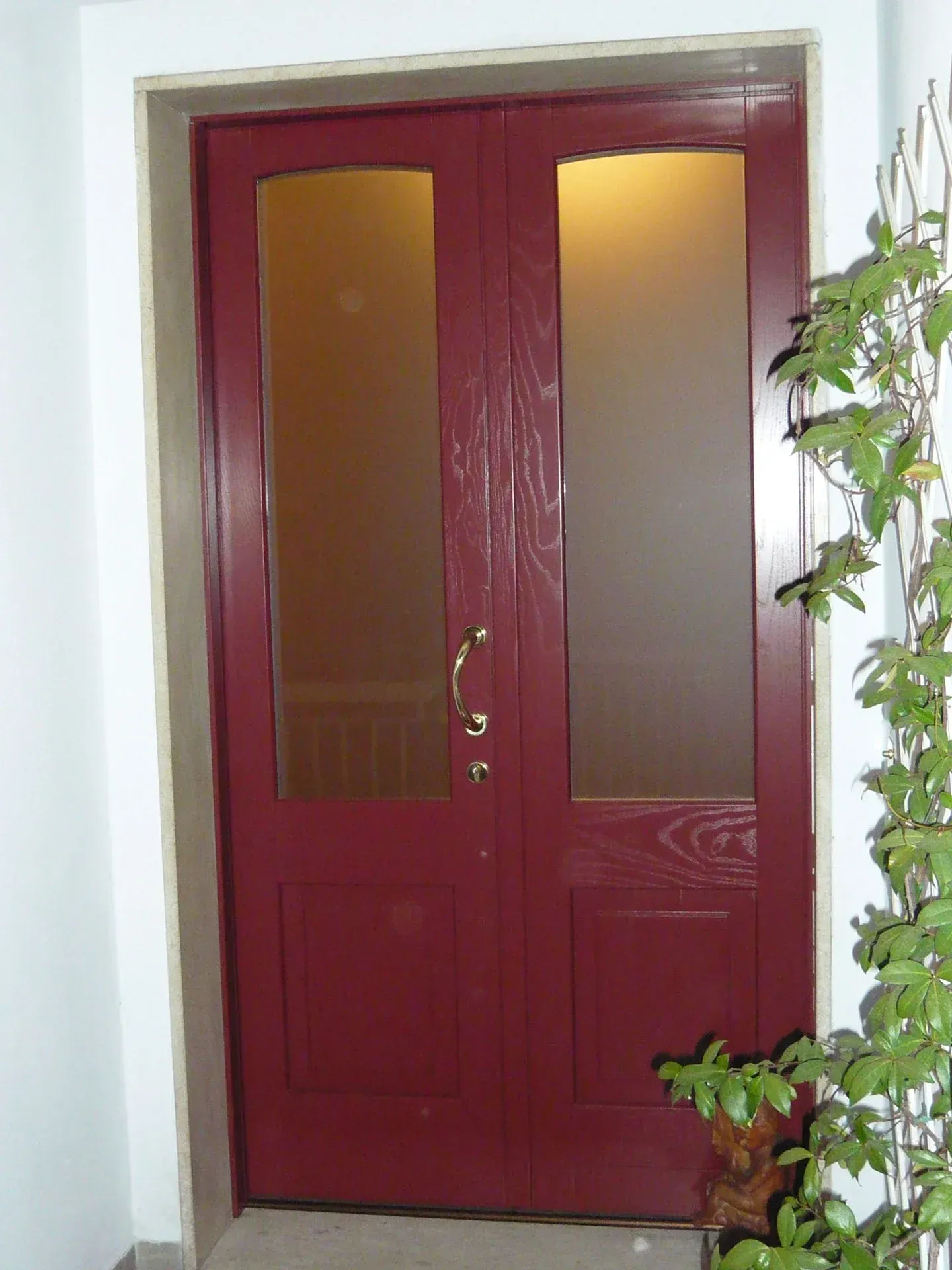Porte doppie rosse con pannelli in vetro smerigliato, maniglia in ottone, telaio bianco.