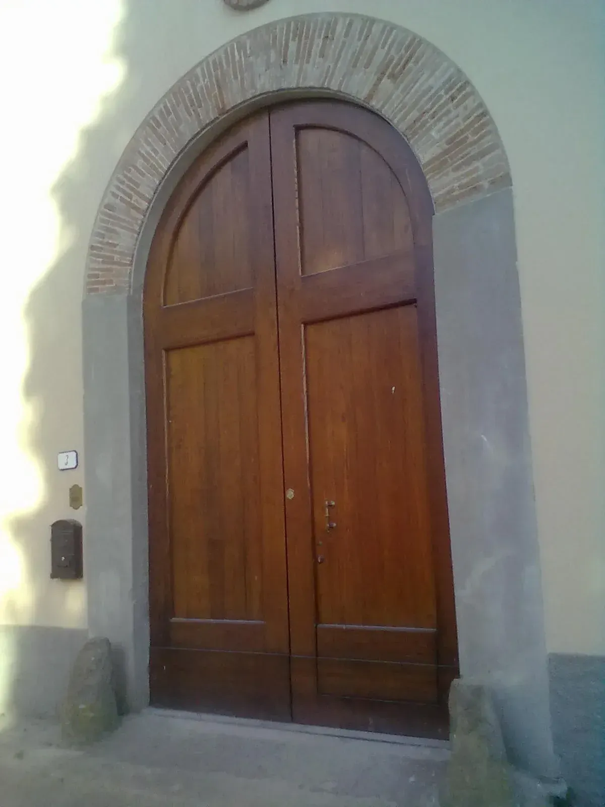 Porta doppia in legno con rifiniture in mattoni ad arco, inserita in un edificio di colore chiaro.