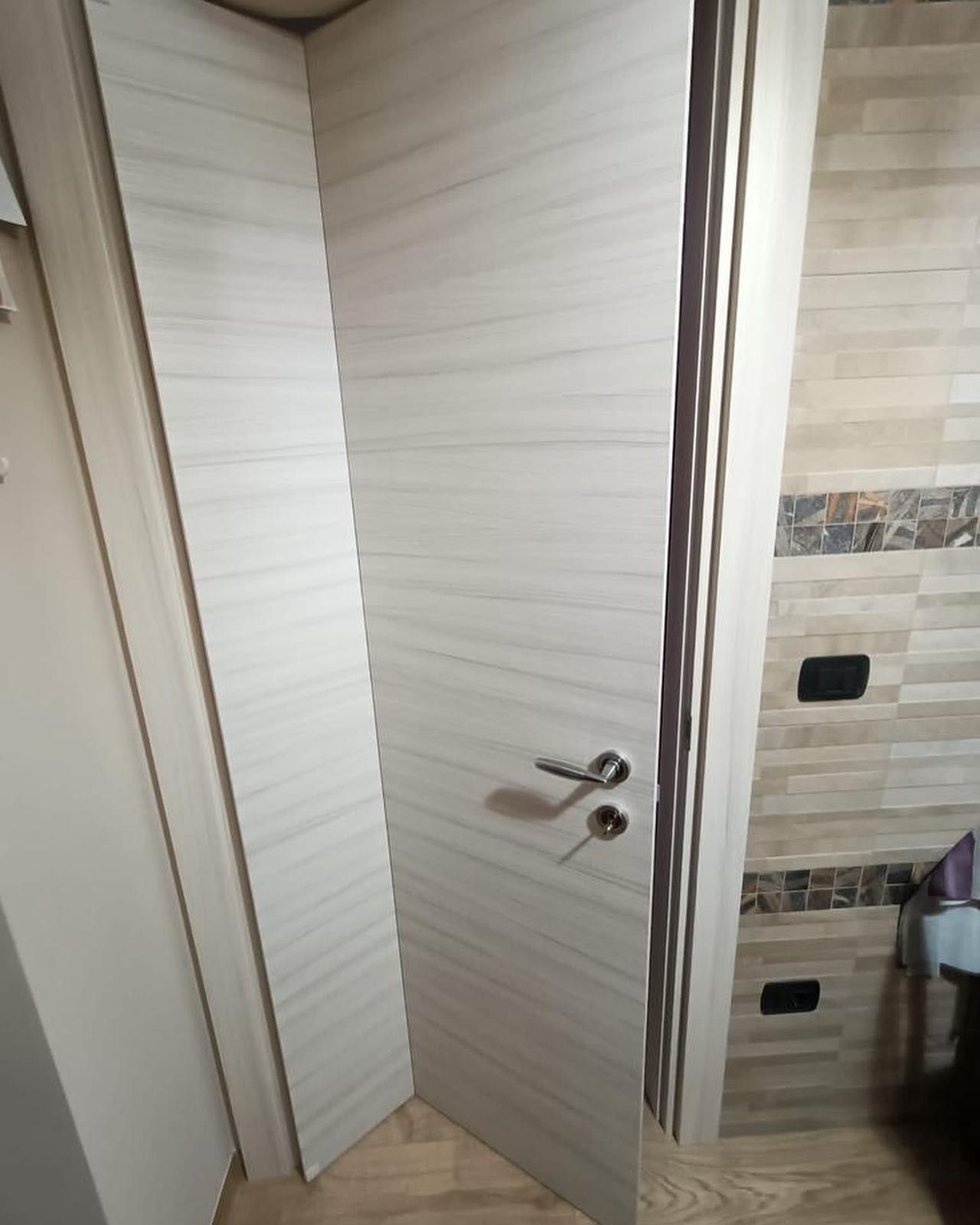 Ingresso in legno ad arco con tre porte a pannelli di vetro, inserito in un edificio in mattoni.