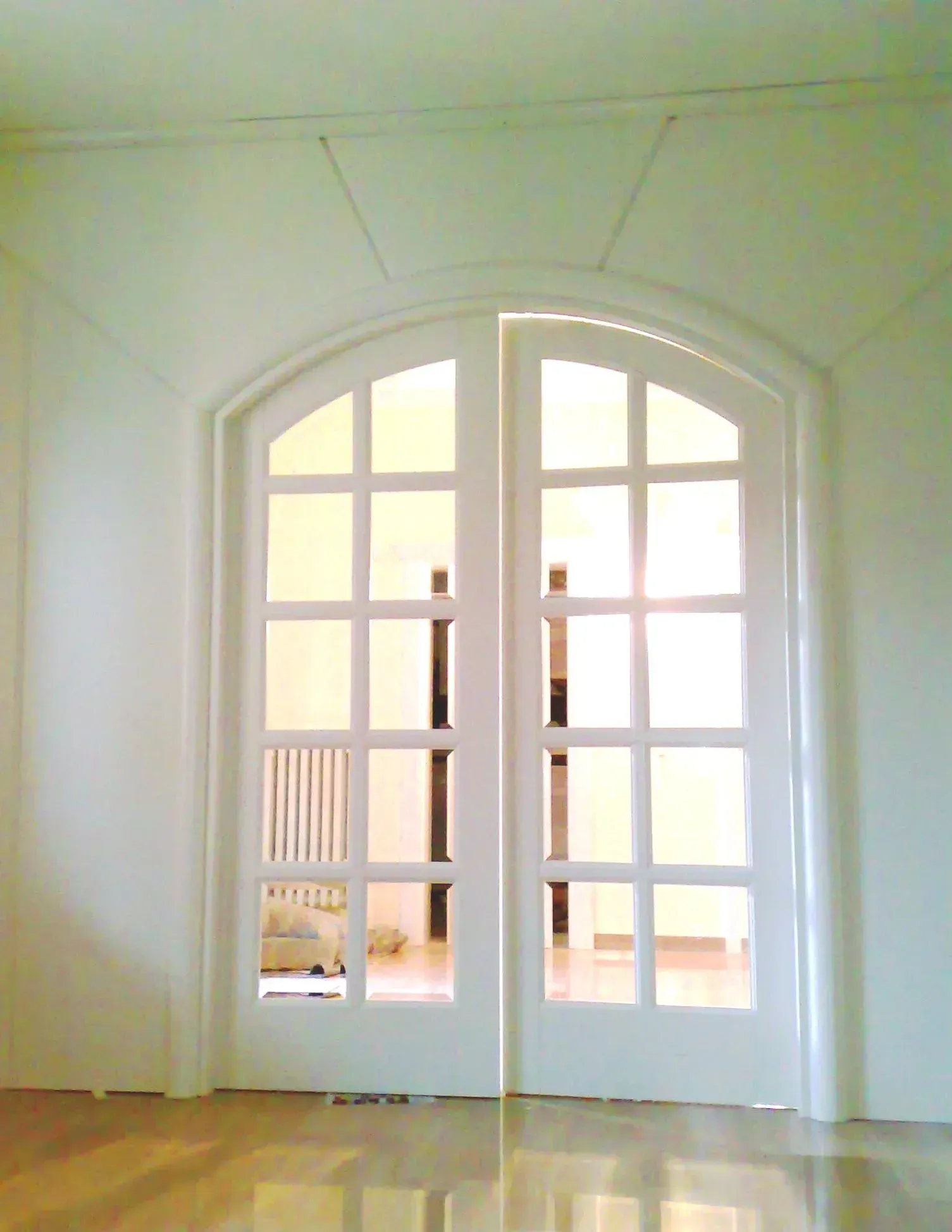 Porte-finestre bianche con parte superiore ad arco, finestre a griglia, che si aprono su una stanza soleggiata.
