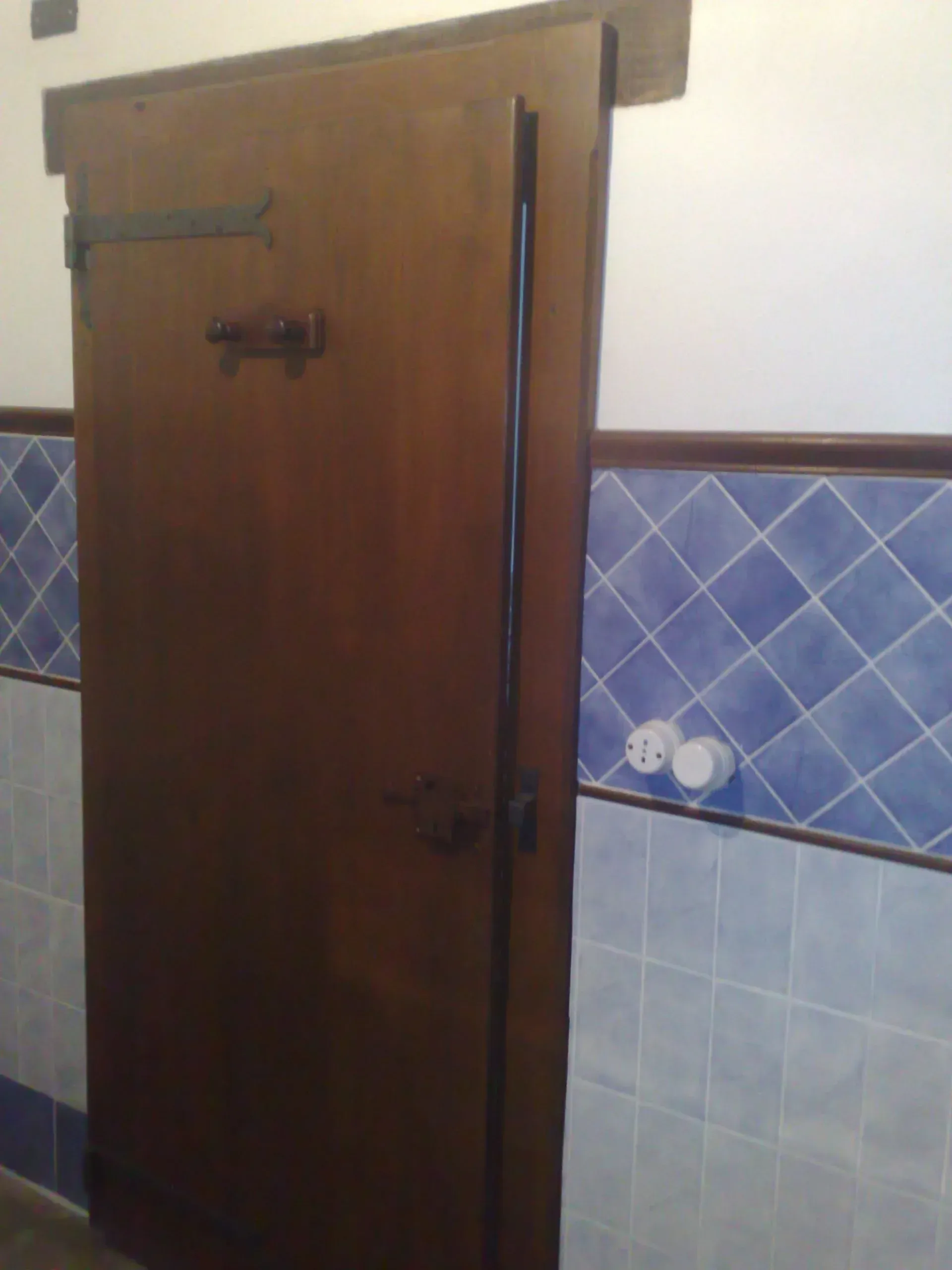 Porta in legno con ferramenta scura, in contrasto con piastrelle blu e parete bianca.