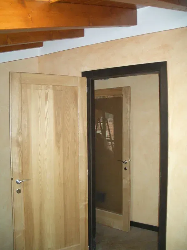 Due porte di legno, una aperta, all'interno di una stanza con pareti color marrone chiaro e travi a vista sul soffitto.