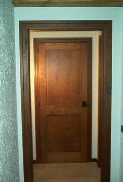 Porta in legno con cornice marrone scuro, inserita in una parete bianca decorata.